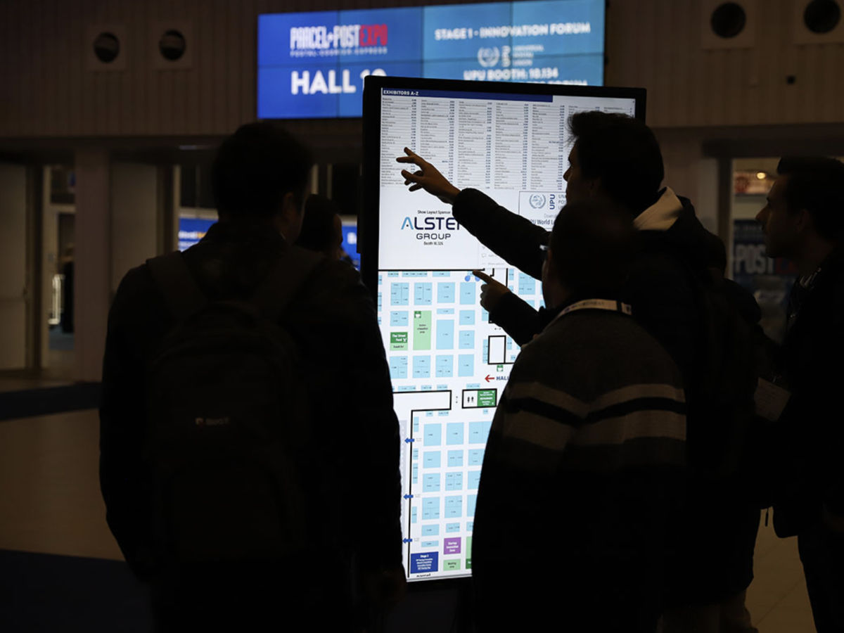 Four people stand in front of an information display. One of them points at the exhibition map. In the background, there is a sign 